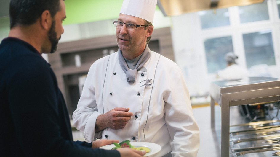 Mann unterhält sich mit Küchenchef und freut sich auf sein Essen.