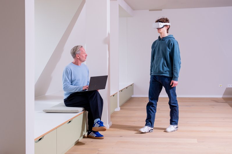 Patient mit VR-Brill auf, Therapeut sitzt mit Laptop daneben