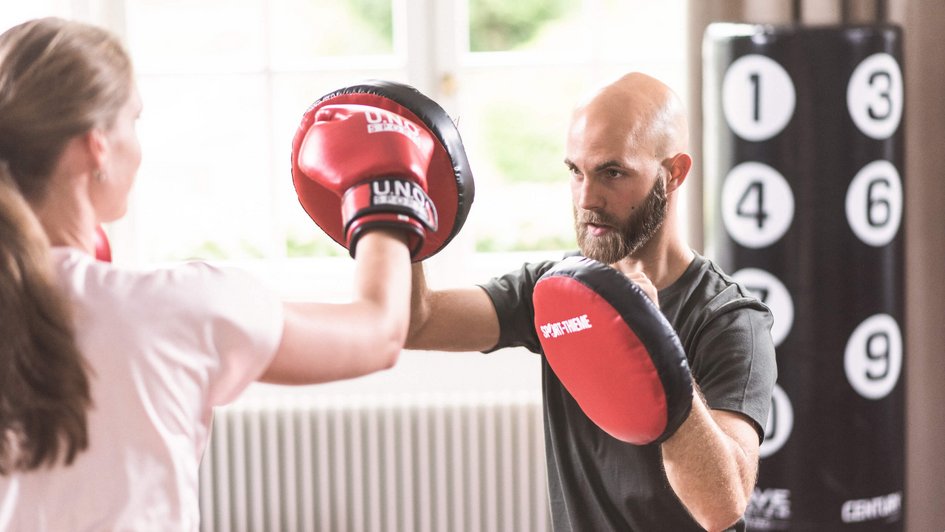 Frau mit Boxhandschuhen schlägt gegen Schlagpolster des Trainers