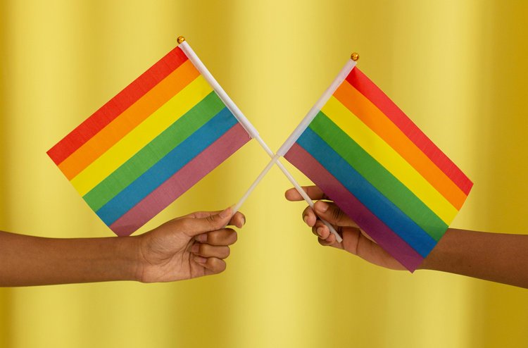 2 Hände vor gelben Hintergrund halten kleine Regenbogenfahnen