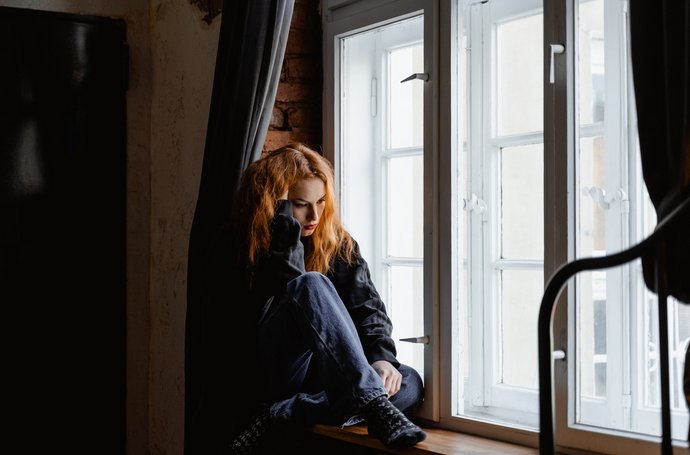Frau sitzt grübelnd am Fenster