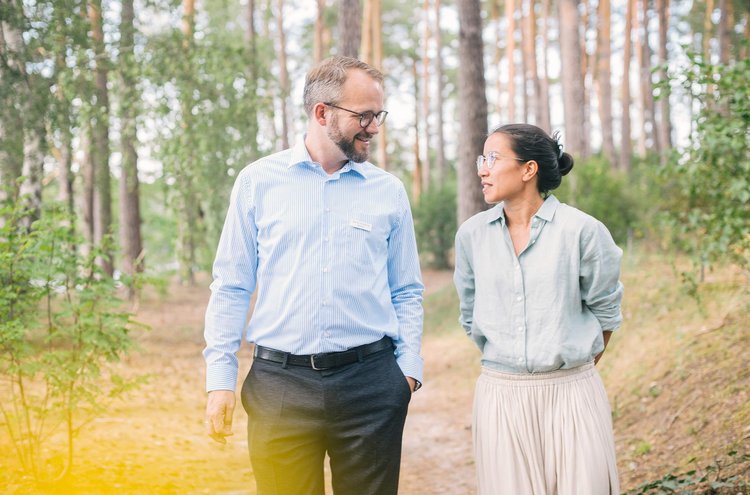 Therapie-Dreiklang Ein Mann und eine Frau spazieren auf einem Pfad durch den Wald und unterhalten sich.