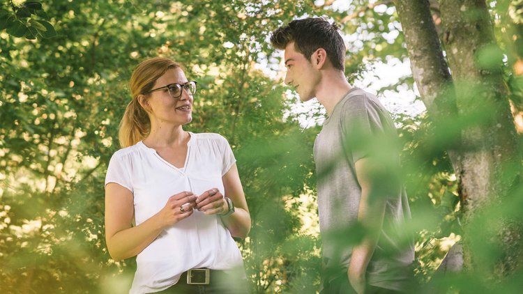 Therapie-Dreiklang Therapeutin spricht während eines Waldspazierganges mit jungem Patienten.