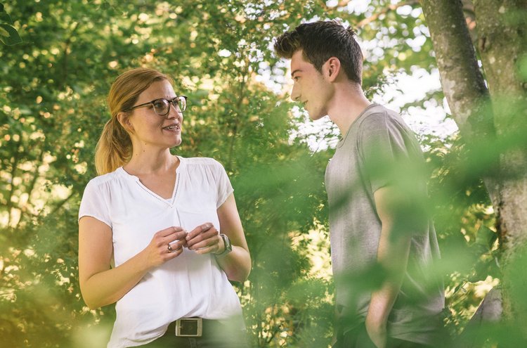 Therapie-Dreiklang Therapeutin spricht während eines Waldspazierganges mit jungem Patienten.