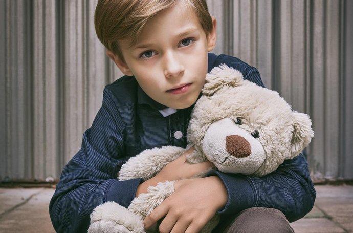 Junge mit Kuscheltier im Arm sitzt traurig da