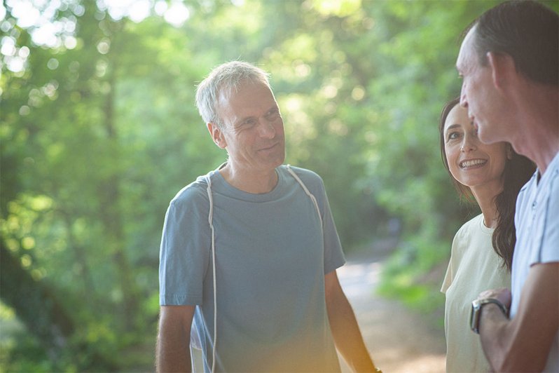Therapeut führt mit einem Mann und einer Frau ein Gespräch, im Hintergrund Bäume.
