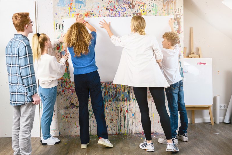 Therapeutinnen bringen mit Patientinnen ein großes weißes Blatt an einer buten Wand an 