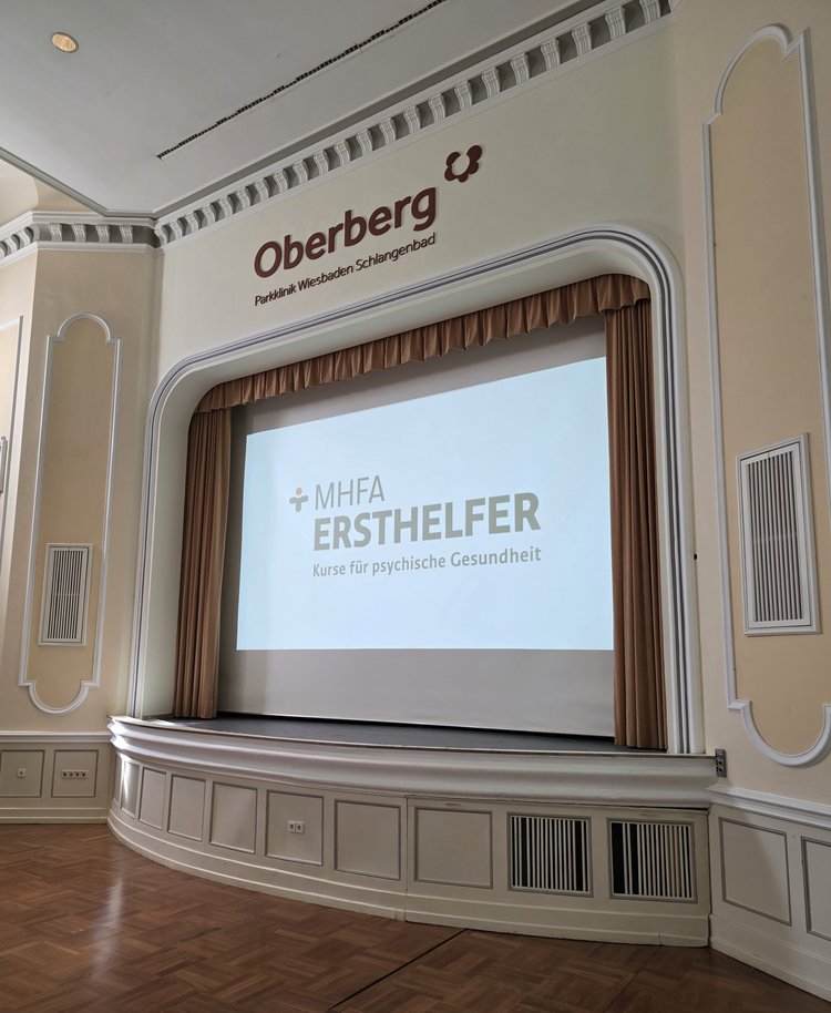 Kultursaal der Oberberg Parkklinik Schlangenbad mit Projektion von MHFA Ersthelfer an der Wand