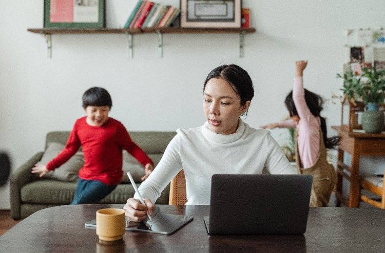 Homeoffice: Mutter am Laptop mit Kindern im Hintergrund