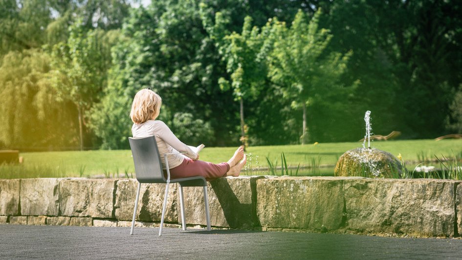 Frau sitzt auf einem Stuhl und legt ihre Füße auf eine Mauer