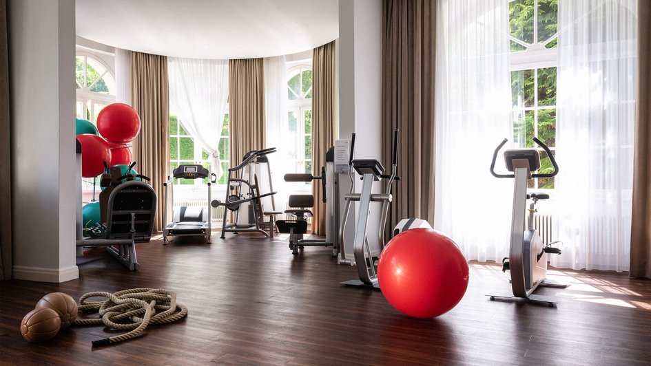 Raum mit großen Fensterfronten und verschiedenen Fitnessgeräten.