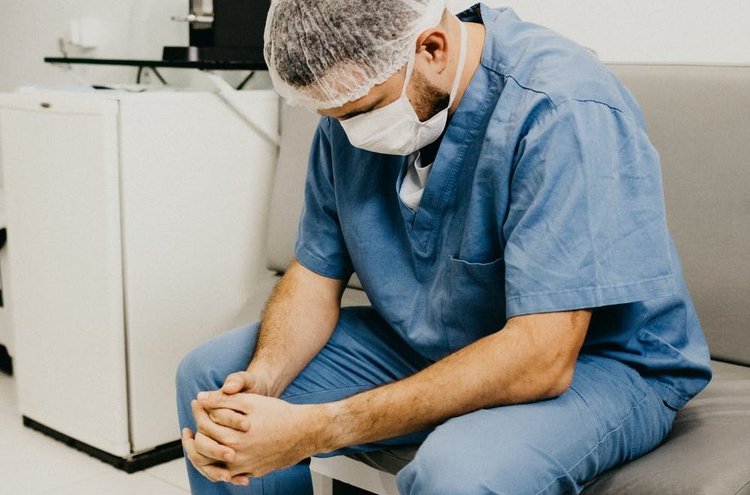 Artikel Folgen von Corona, Krankenpfleger sitzt auf einem Stuhl mit hängendem Kopf