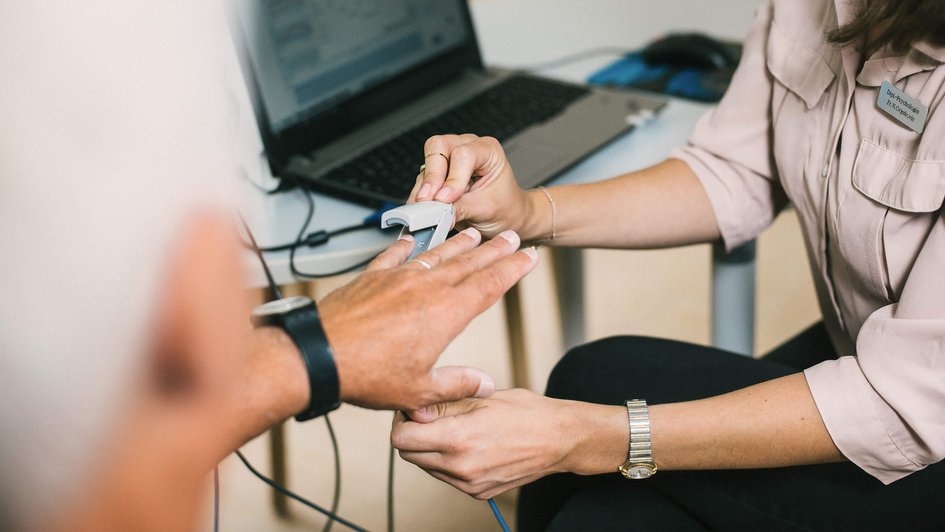 Therapie-Dreiklang Eine Ärztin steckt einem Patienten einen elektrischen Pulsmesser-Clip an den Finger.