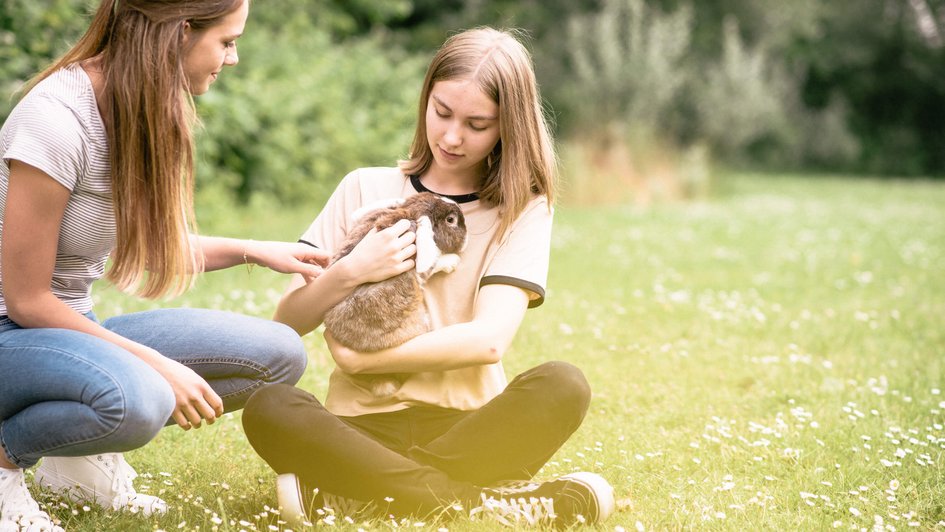 Zwei junge Frauen auf einer Wiese mit einem Hasen