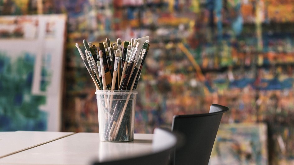 Becher mit Pinseln vor einer bunten Wand