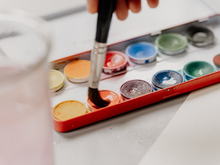 Ein Pinsel nimmt Orange Farbe aus einem Farbkasten auf